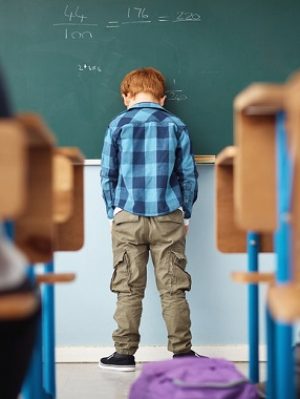 Rear view shot of an elementary school boy leaning with his head on the chalkboard in class